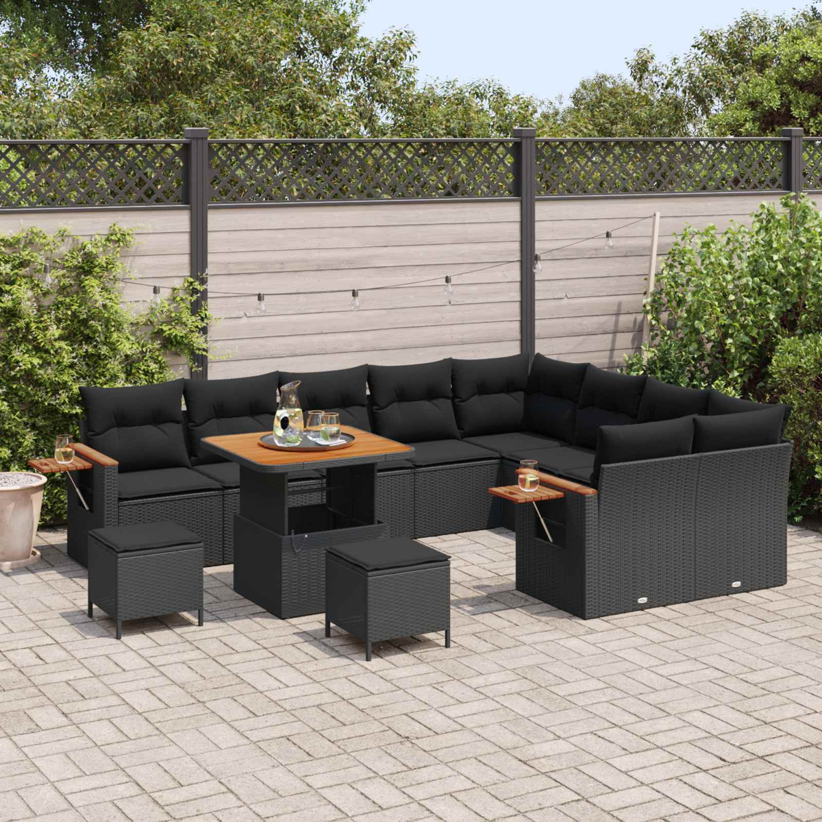 Ein dunkles Rattan-Lounge-Set mit schwarzen Kissen und einem Tisch auf einer gepflasterten Terrasse.