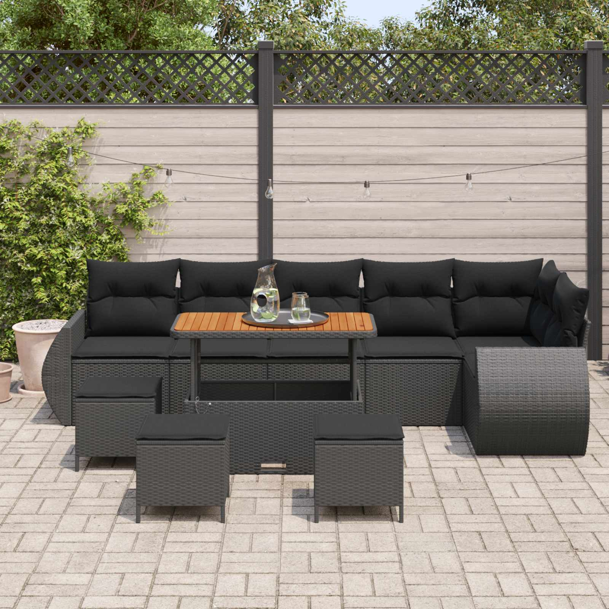Un conjunto de sofá de exterior oscuro con mesa y taburetes en un patio pavimentado.