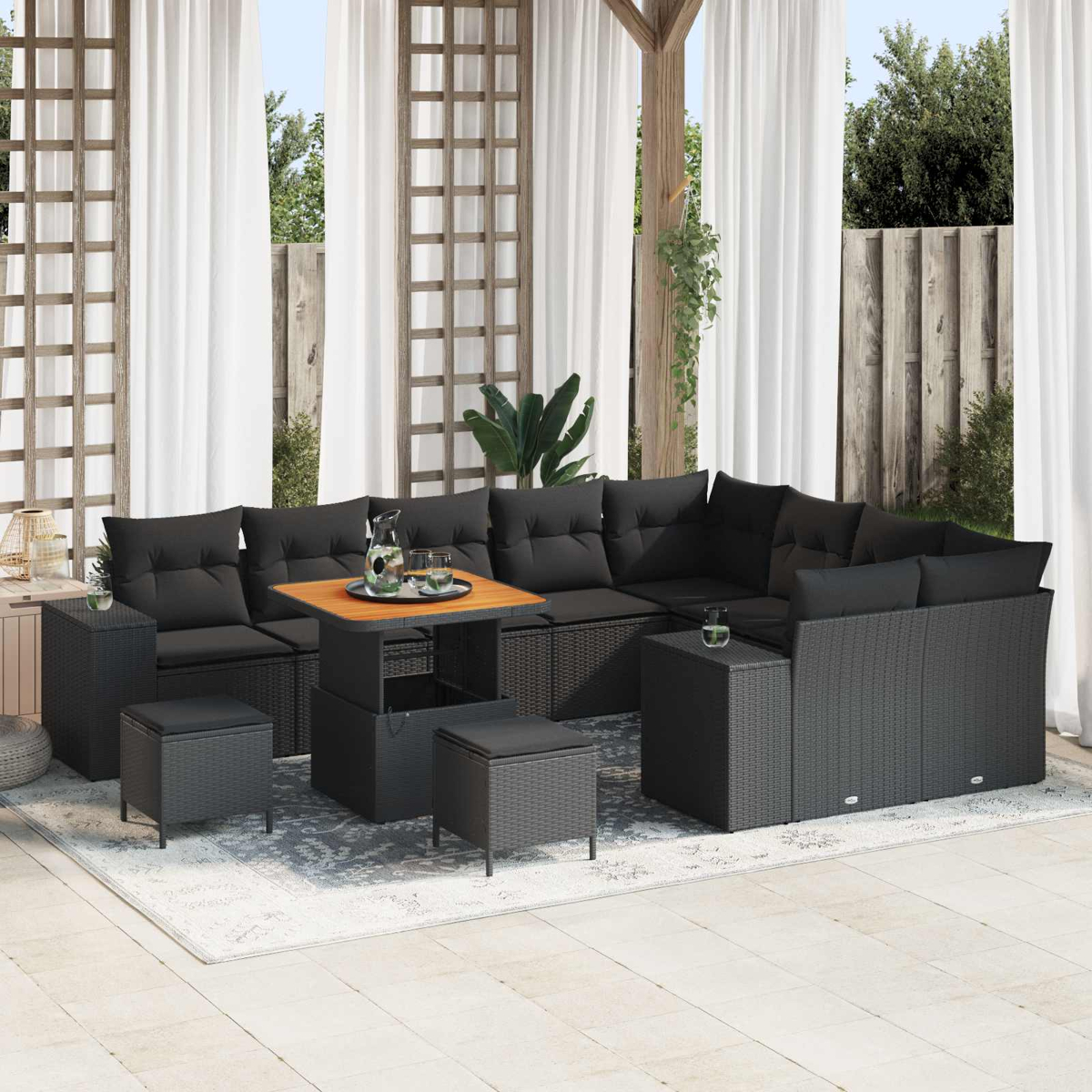 Ein schwarzes Lounge-Set auf einer Terrasse mit weißen Vorhängen und Holzbalken.