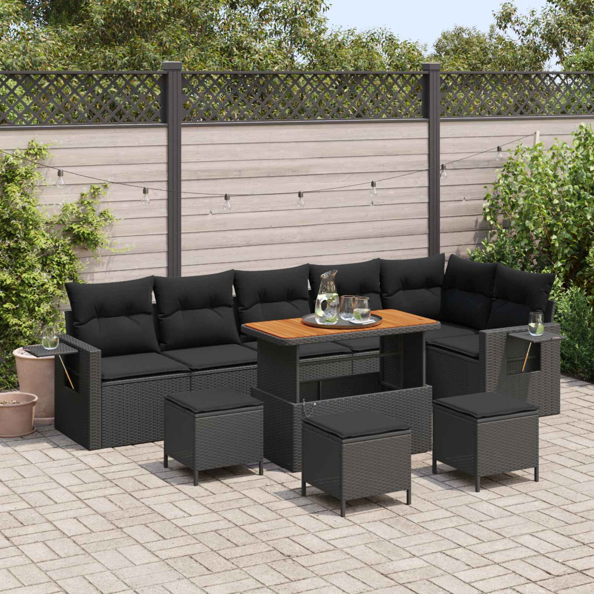 Gartenmöbel-Set mit dunklen Kissen, Tisch und Hockern auf einer Terrasse.