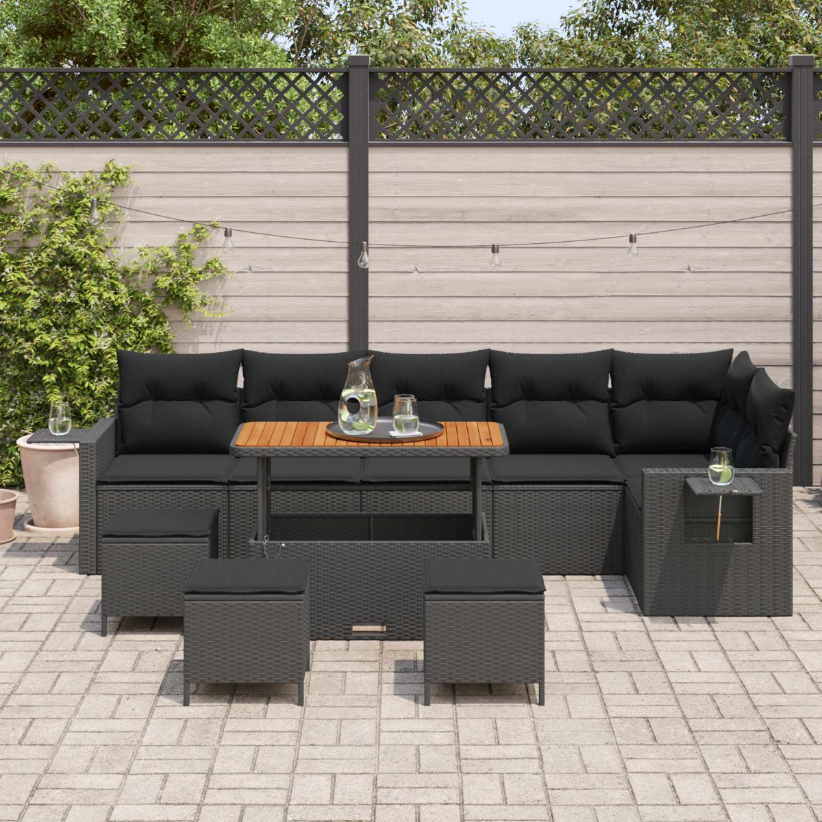 Dunkelgraue Rattan-Lounge-Möbel mit schwarzen Kissen, Holztisch und Lichtern.