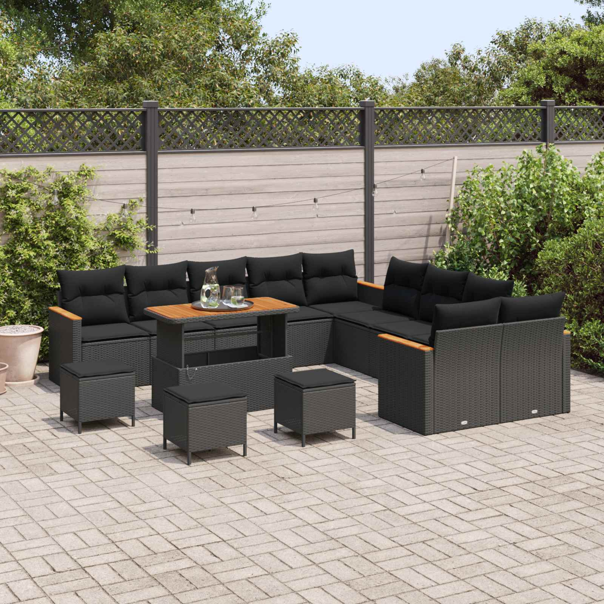 Dunkelgraue Gartenlounge mit schwarzen Kissen und Holzakzenten auf einer gepflasterten Terrasse.