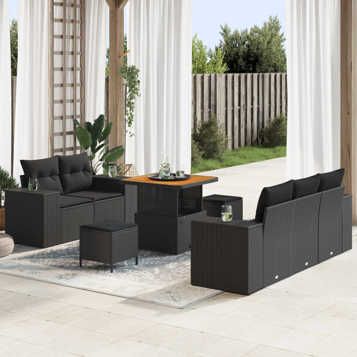 Dunkelgraue Rattan-Gartenmöbel mit schwarzen Kissen auf einer Terrasse mit Holzzaun.