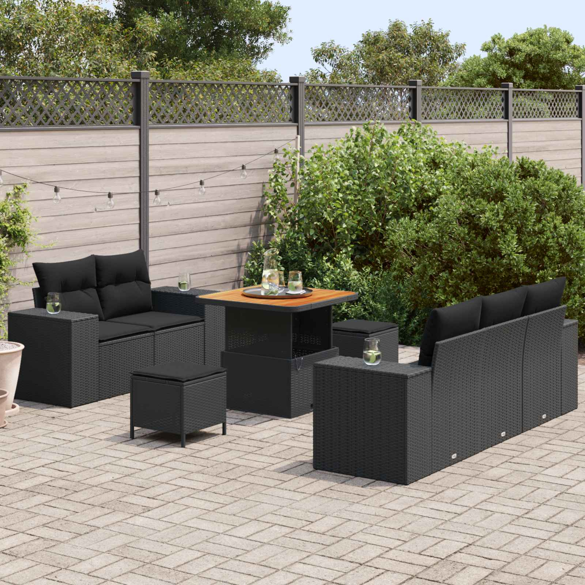 Dunkles Rattan-Möbelset auf Kopfsteinpflaster, mit Holztisch, Sofas und Hockern.