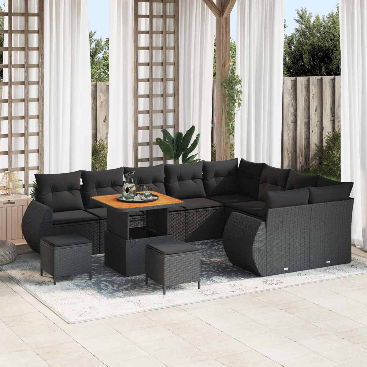Ein schwarzes Rattansofa mit Tisch und Hockern auf einer Veranda.