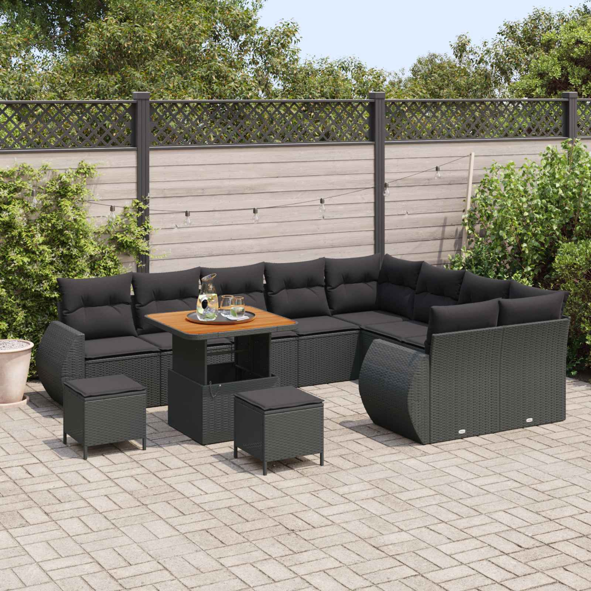 Ein graues Rattan-Lounge-Set mit schwarzen Kissen und einem Holztisch auf einer gepflasterten Terrasse.