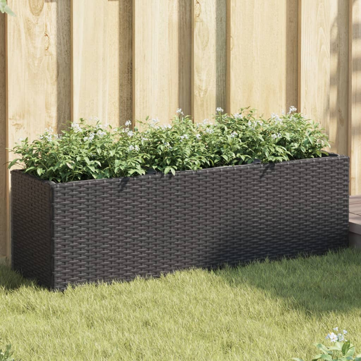 Fioriera in rattan marrone scuro con piante verdi e fiori bianchi all'aperto.