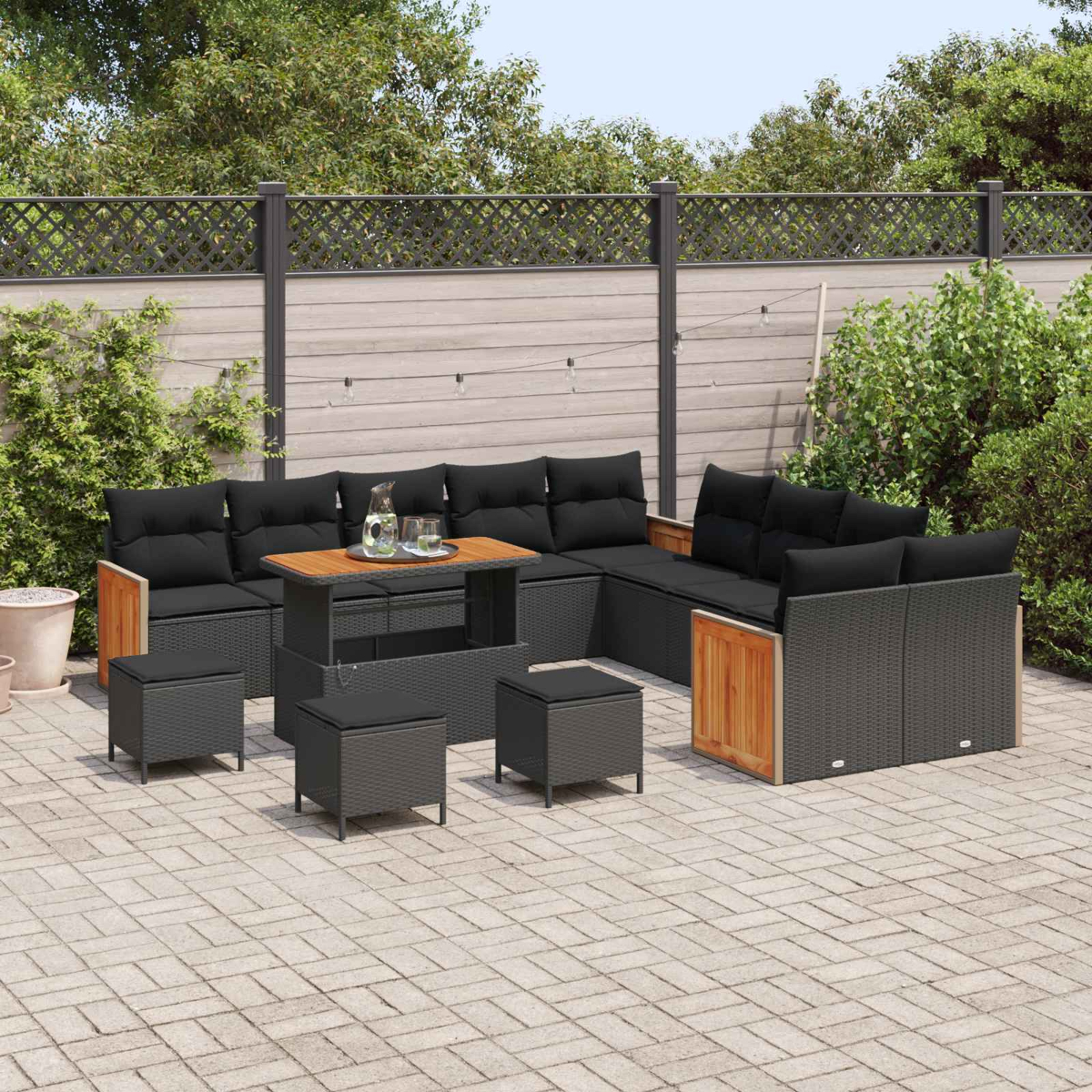 Gartenlounge mit schwarzen Kissen und Holzakzenten auf einer gepflasterten Terrasse.