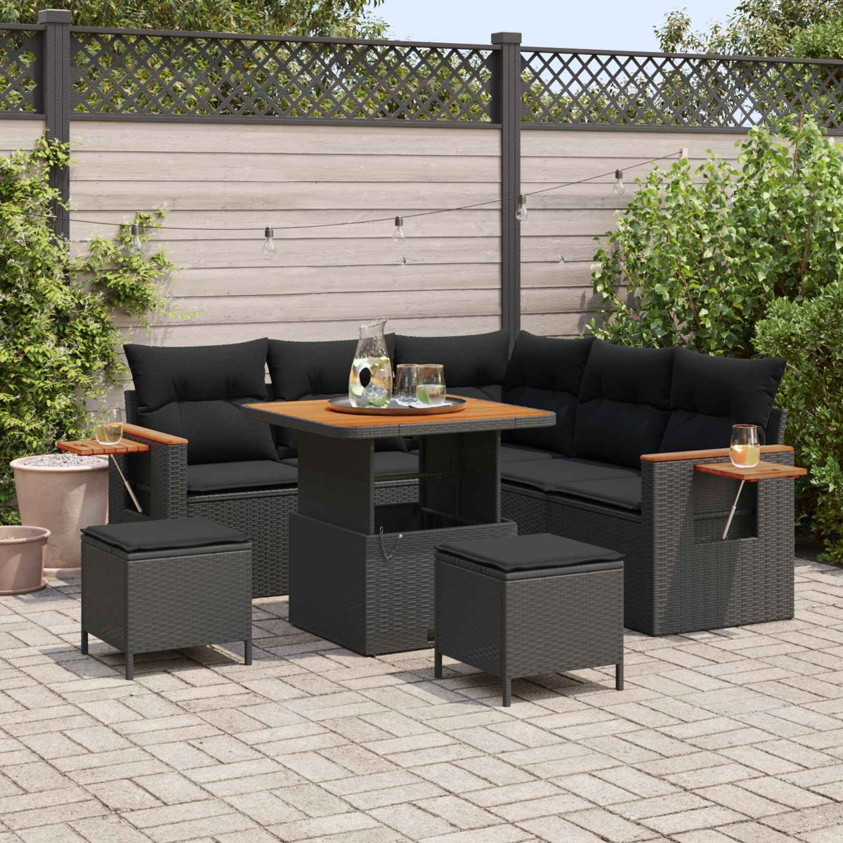 Gartenlounge mit schwarzen Kissen, Holztisch, Hockern und Lichtern.