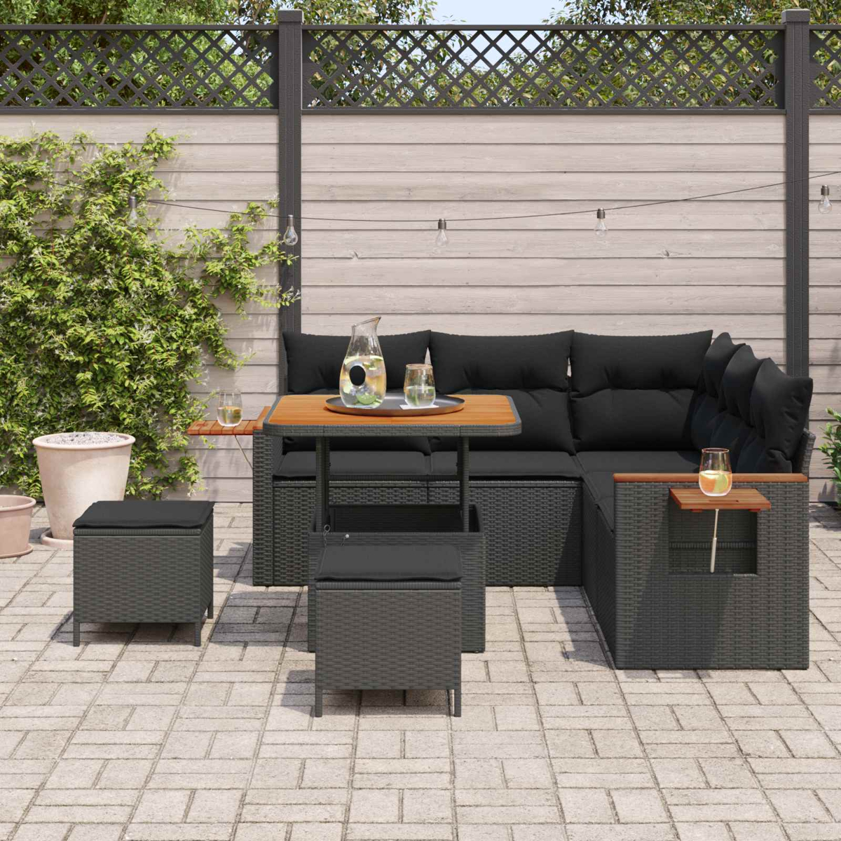Dunkelgraue Rattan-Gartenlounge mit schwarzen Kissen, Holztisch und Hockern.