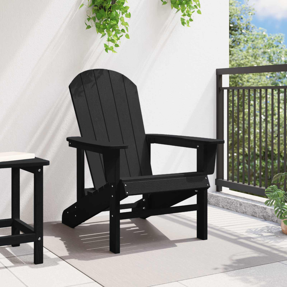 Schwarzer Adirondack-Stuhl auf einer Terrasse mit einem kleinen Tisch und Pflanzen im Hintergrund.