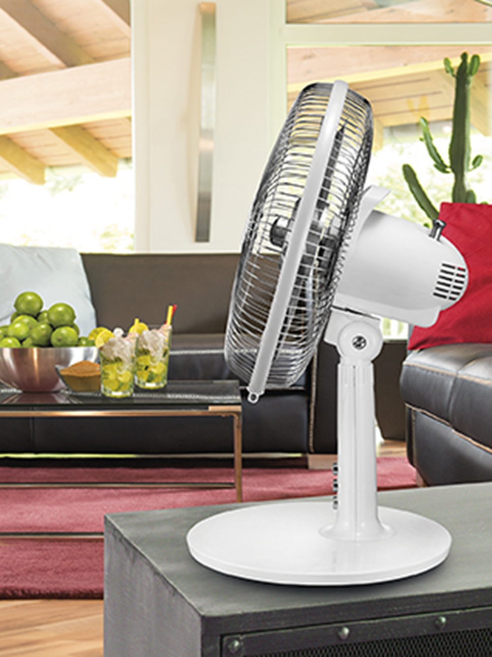 Biały wentylator stoi na stole przed kanapą z zielonymi jabłkami i napojami.