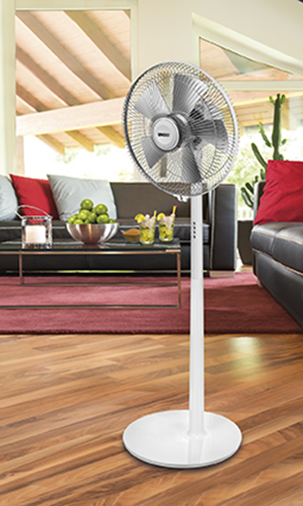 Biały wentylator stojący znajduje się w salonie z sofami i stolikiem kawowym.