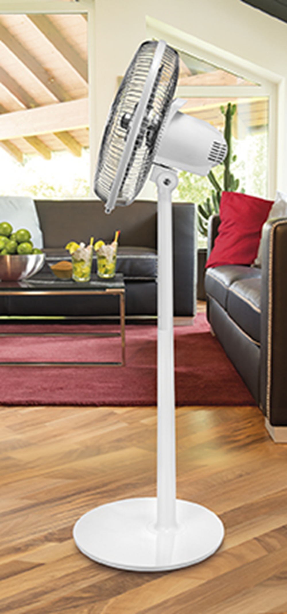 Biały wentylator stojący na drewnianej podłodze przed salonem.