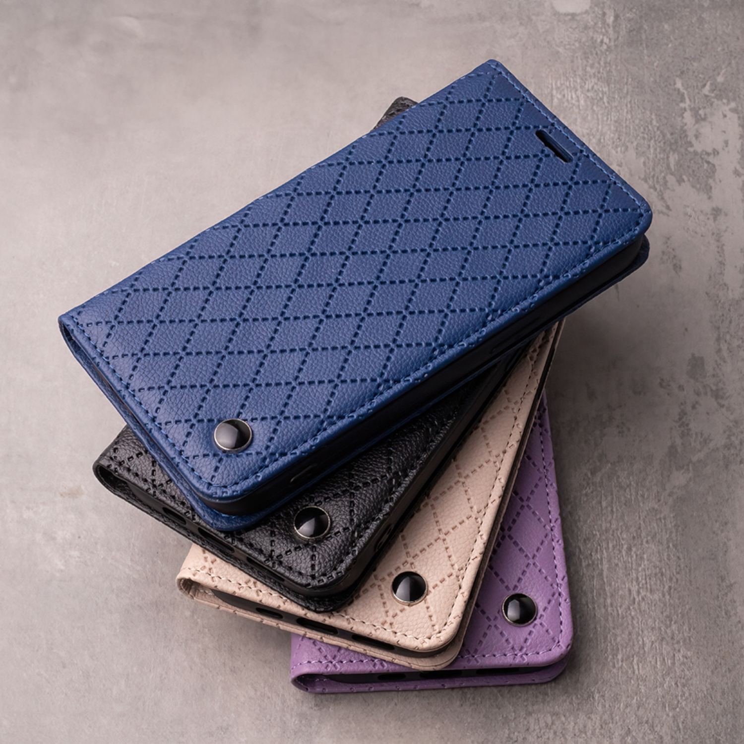 Vier gesteppte Handyhüllen in Blau, Schwarz, Beige und Lila auf grauem Hintergrund.