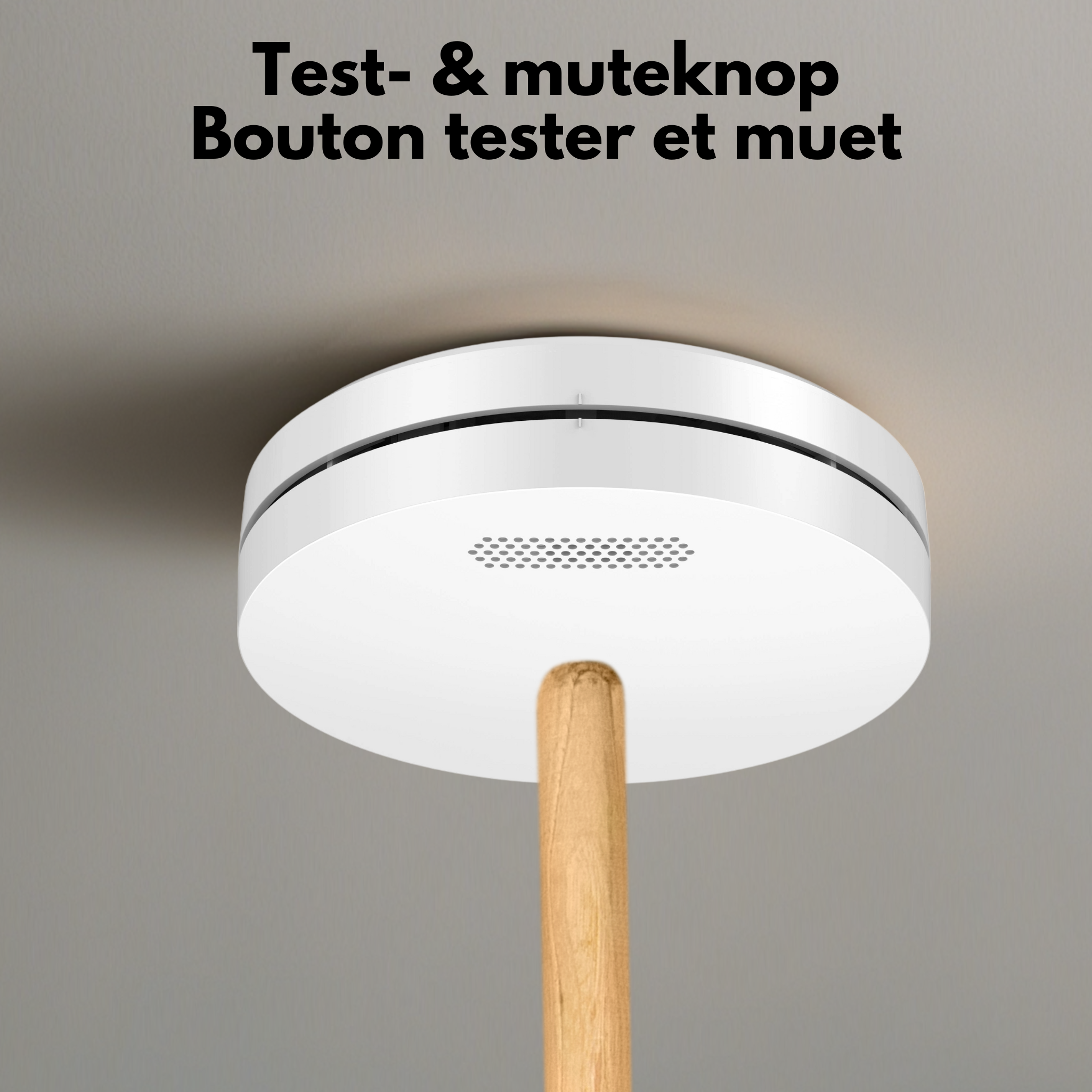 A white smoke detector hangs from a ceiling. A wooden stick touches it.