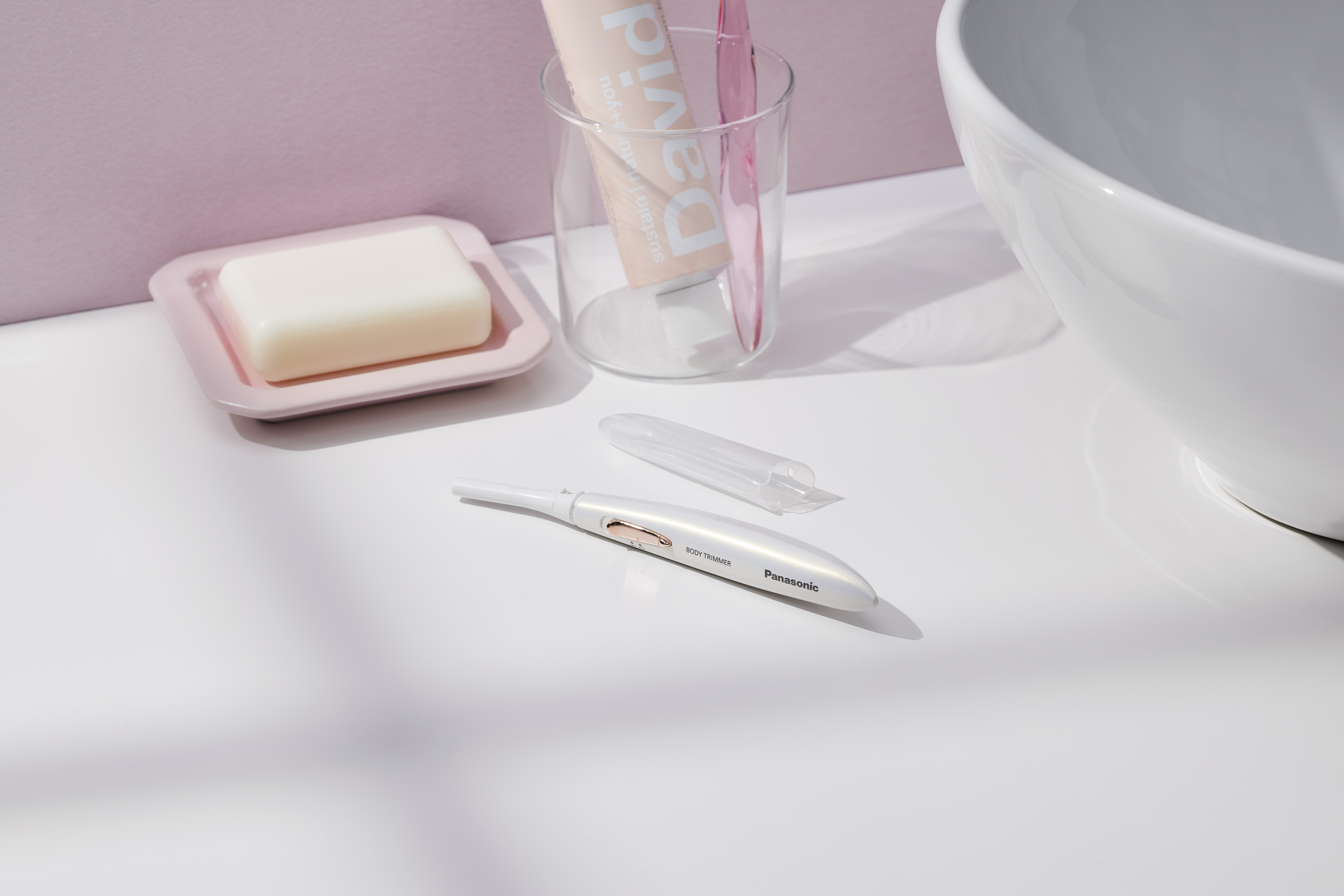 Ein weißer Panasonic Body Trimmer mit rosa Seifenschale und Zahnbürste.