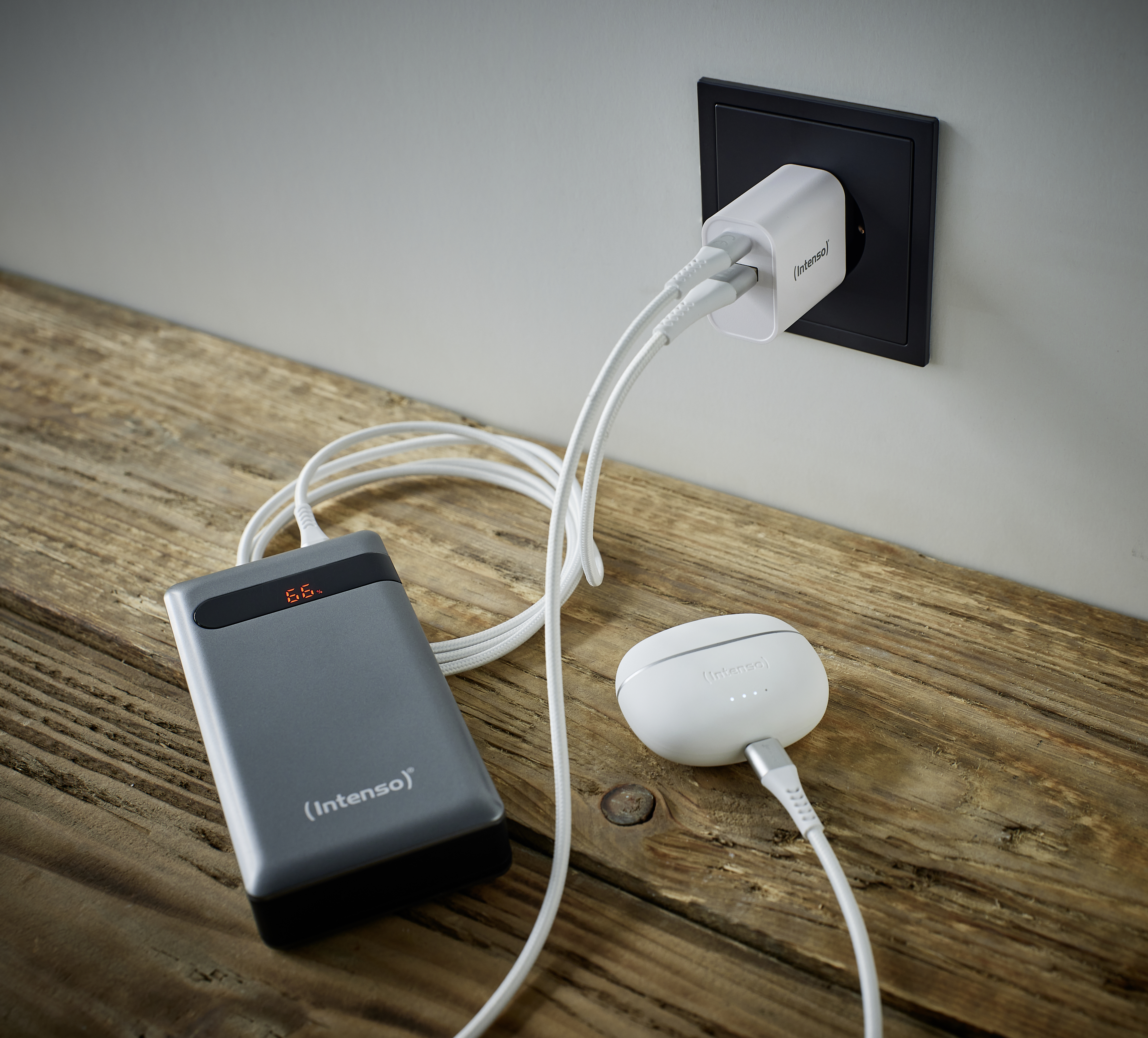 Un adattatore di corrente carica un power bank e auricolari su un tavolo di legno.