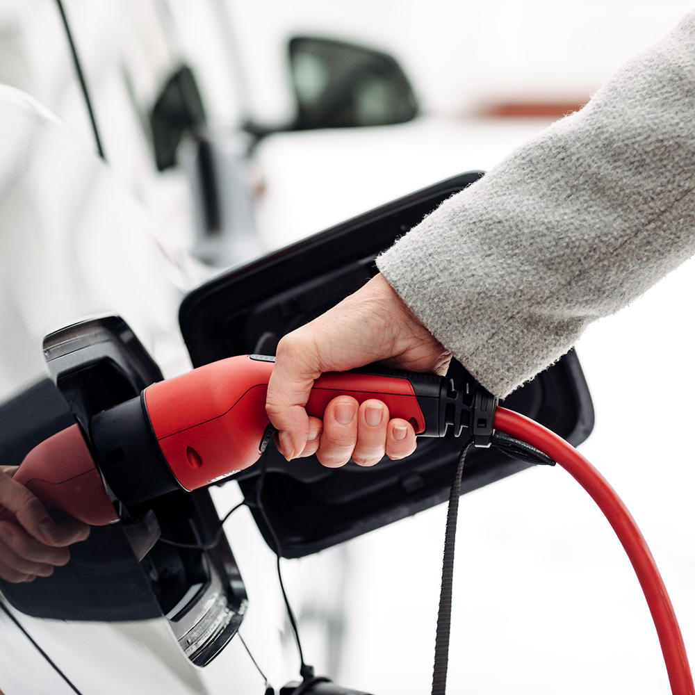 Una mano tiene un connettore di ricarica rosso per caricare un'auto elettrica.