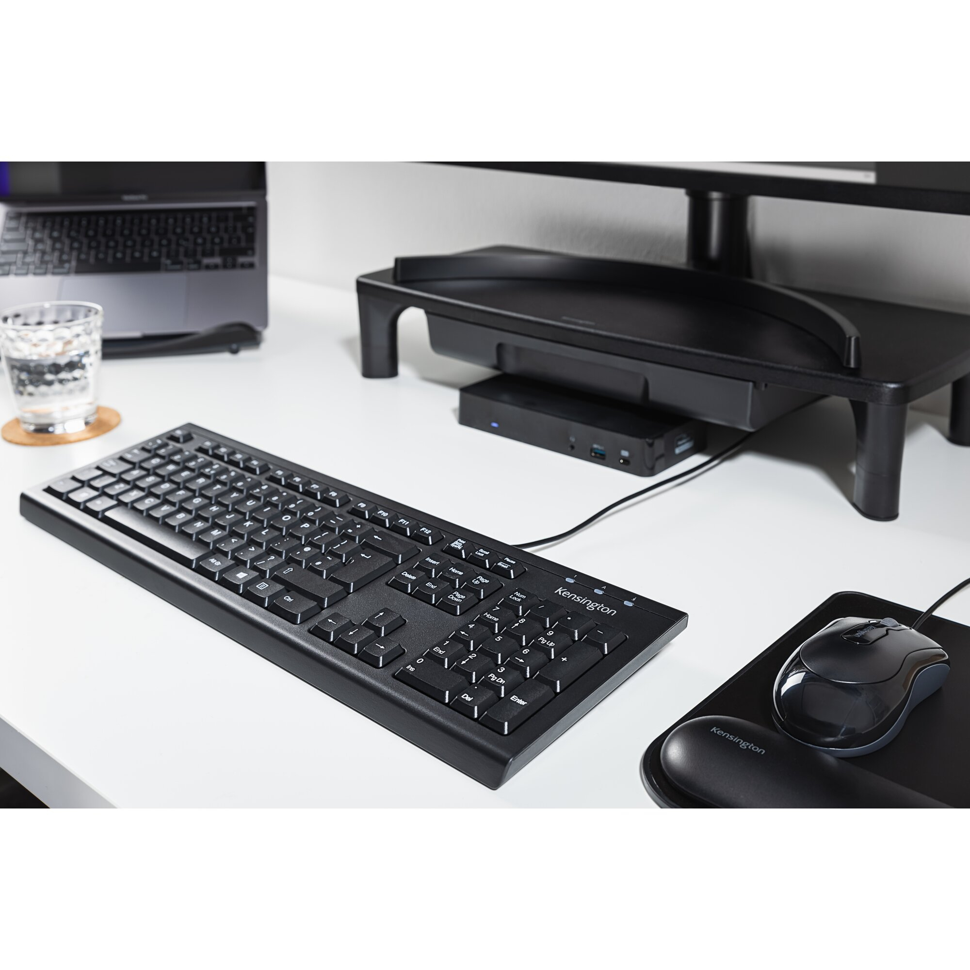 Schreibtisch mit Tastatur, Maus, Glas Wasser und Laptop.