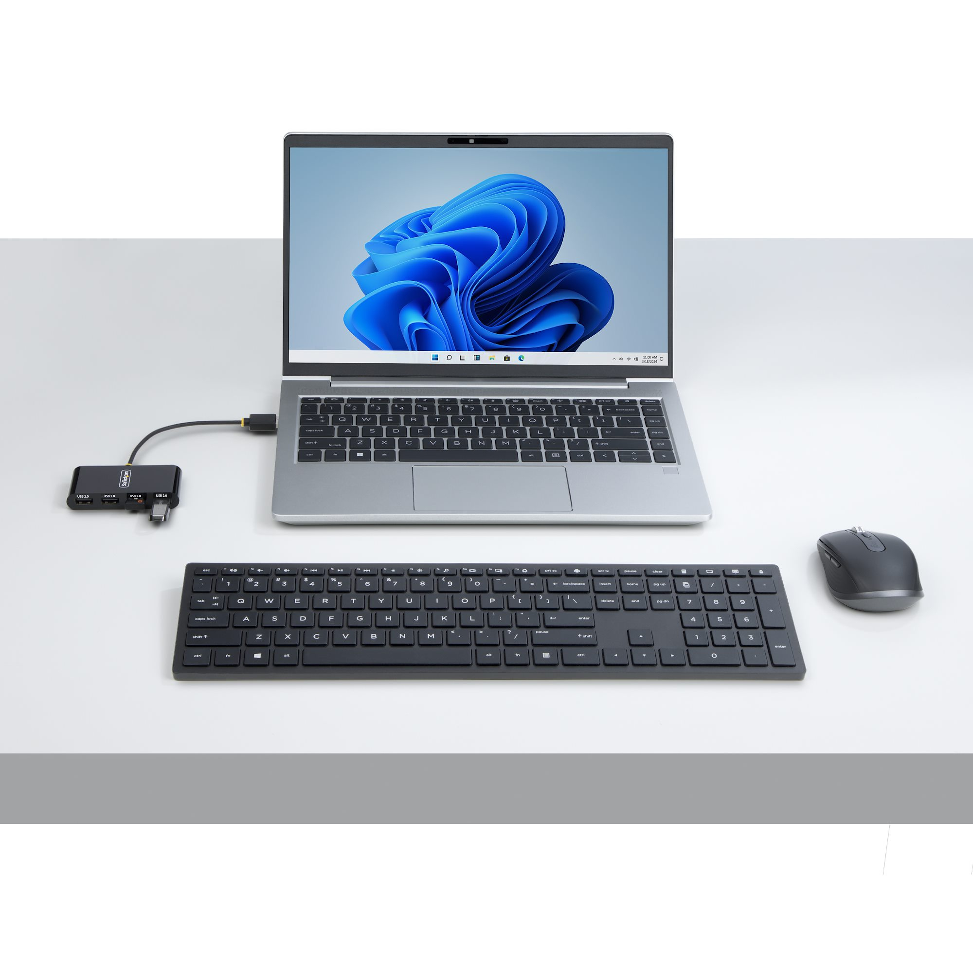 Un laptop con sfondo blu, tastiera, mouse e hub USB su un tavolo.