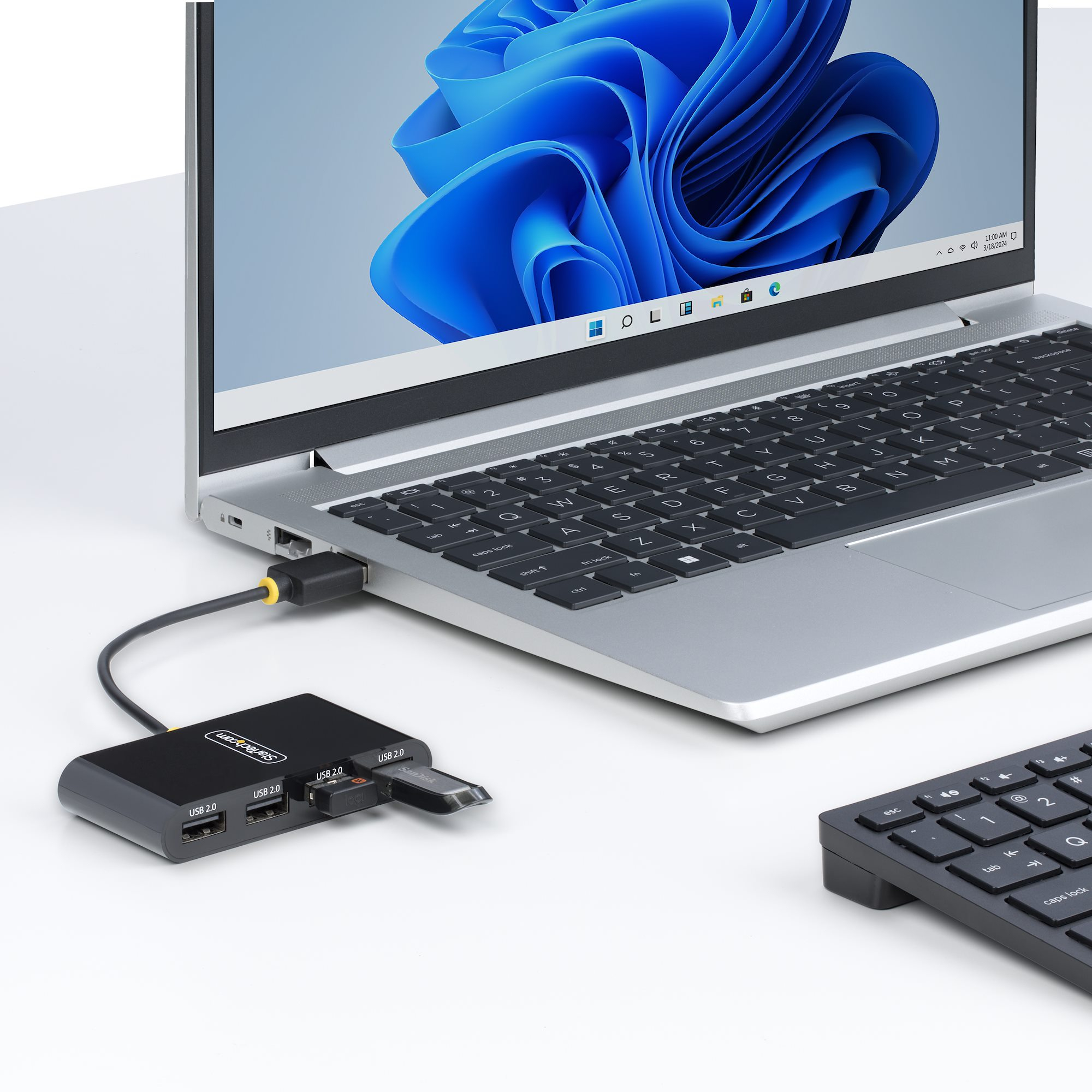 Un hub USB nero con un'unità flash SanDisk è collegato a un laptop argentato.