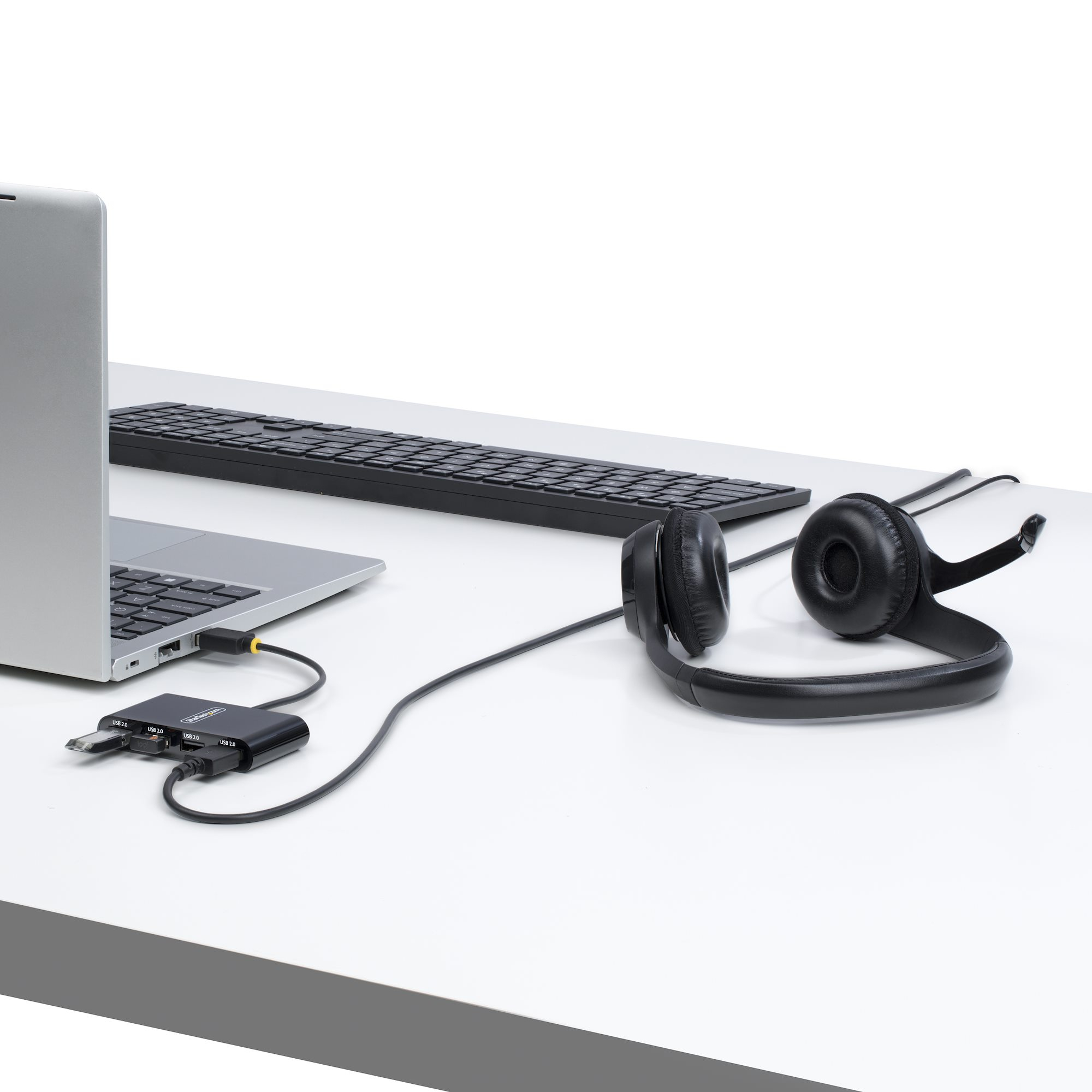 Un laptop, tastiera, cuffie e hub USB disposti su una scrivania bianca.