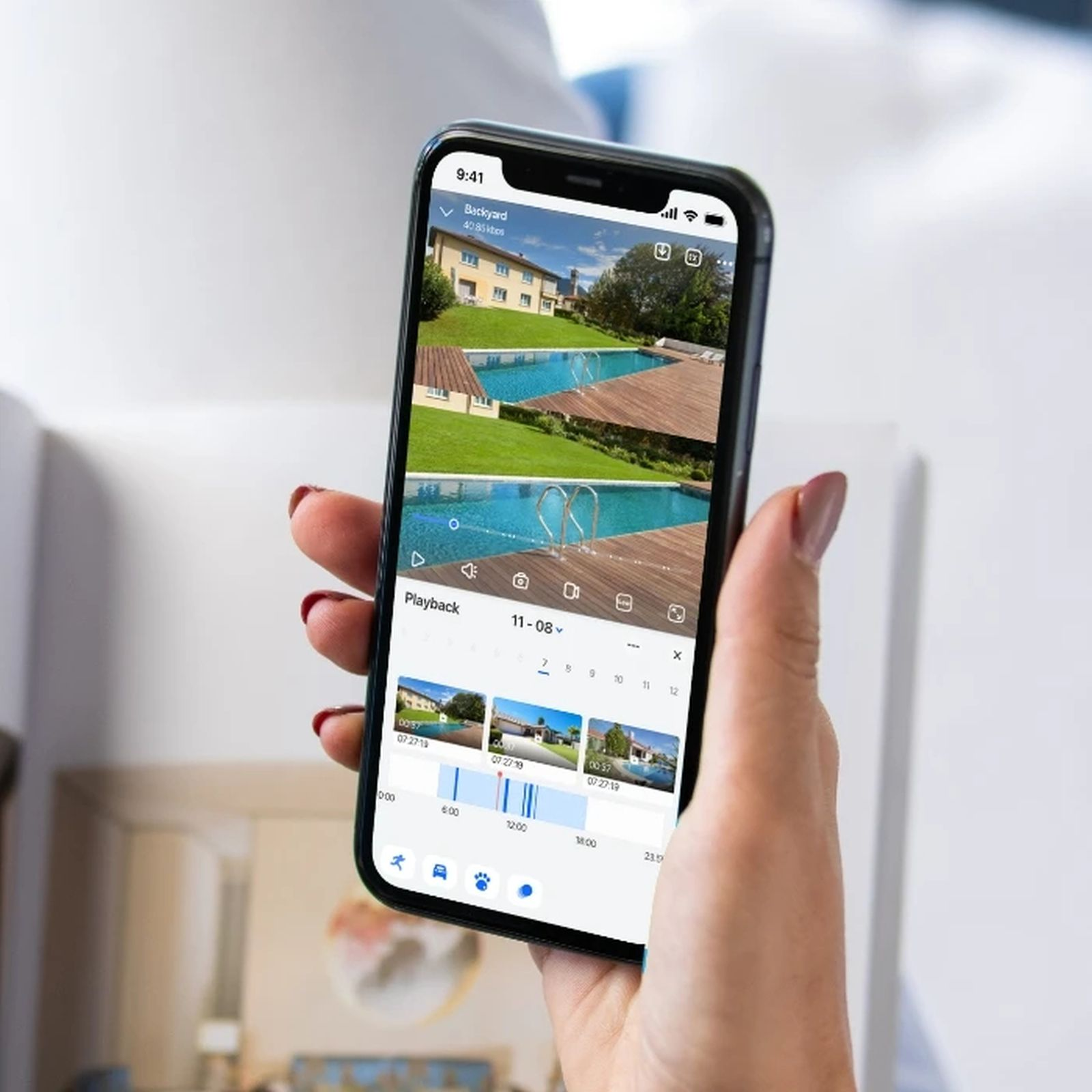 Eine Hand hält ein Smartphone mit einer Überwachungs-App, die einen Garten mit Pool zeigt.