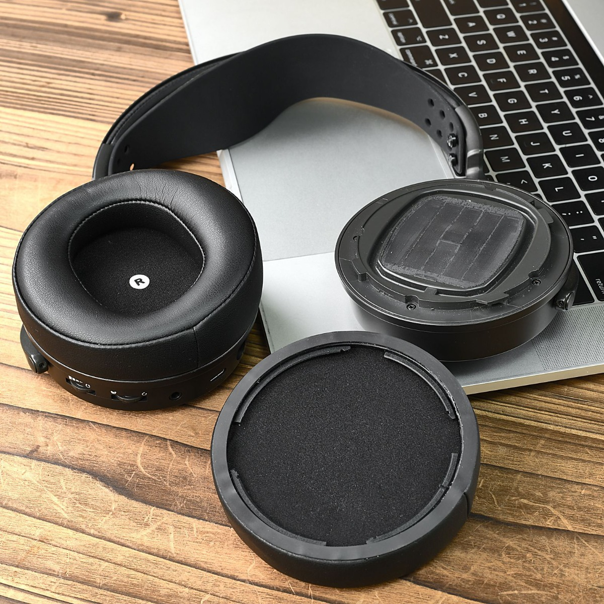 Auriculares negros desmontados y portátil sobre mesa de madera.