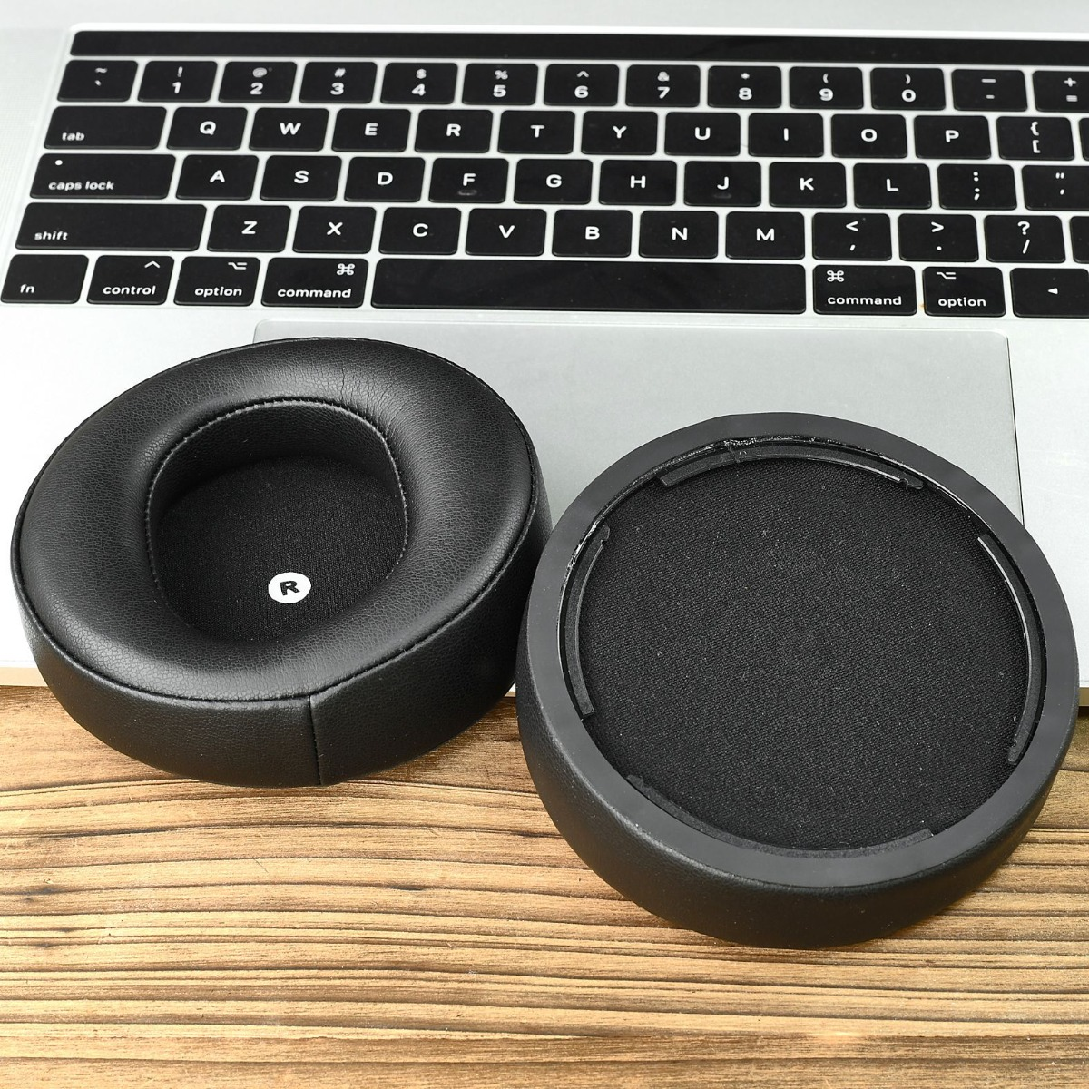 Dos almohadillas negras para auriculares descansan sobre un teclado. Una almohadilla tiene una etiqueta R.