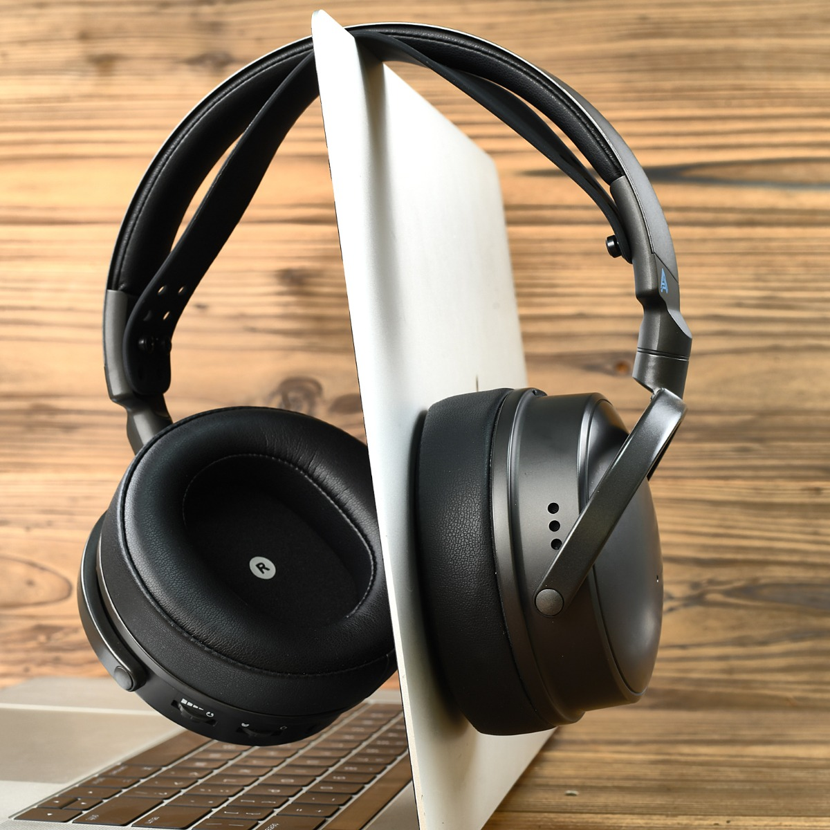 Auriculares negros apoyados en un portátil abierto, sobre fondo de madera.