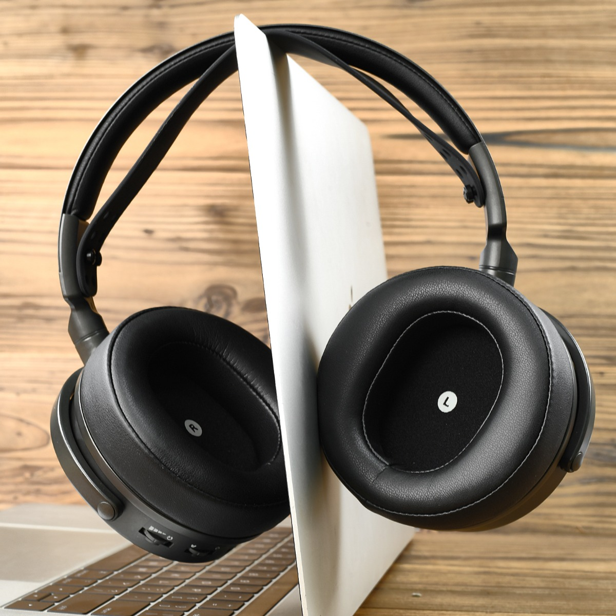 Auriculares negros descansan sobre un portátil abierto con fondo de madera.