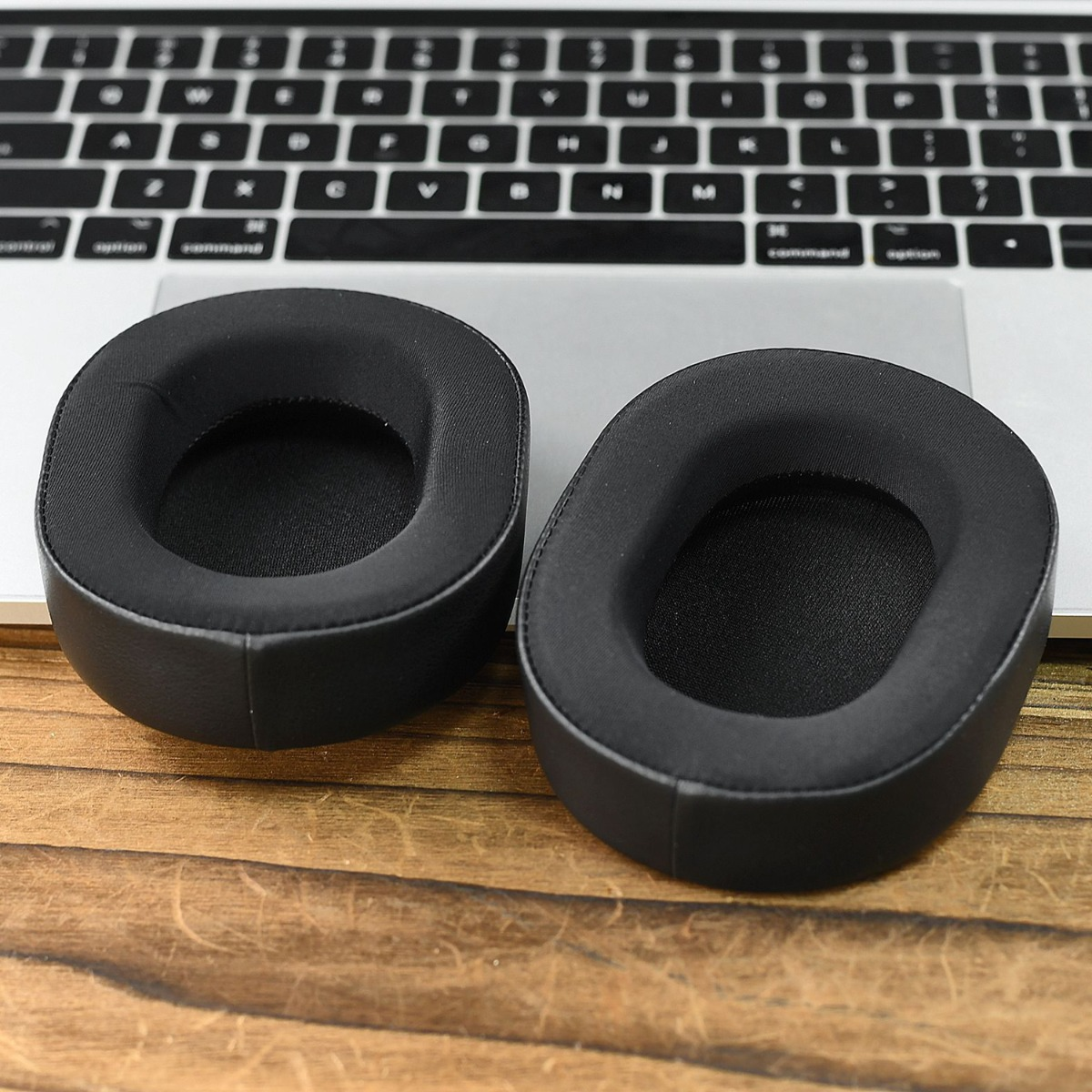 Dos almohadillas negras para auriculares descansan sobre un teclado y mesa de madera.