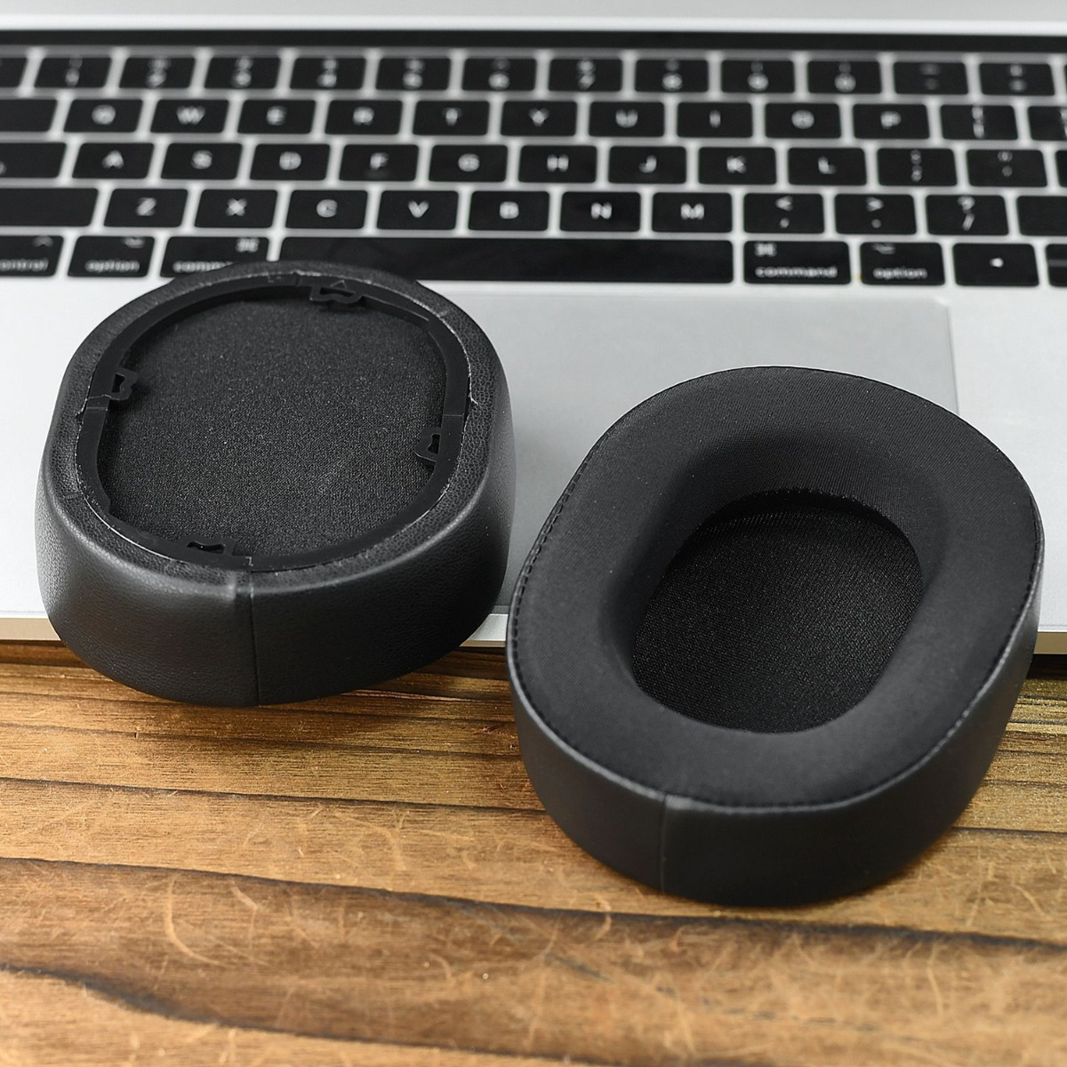 Dos almohadillas negras para auriculares están sobre un teclado de portátil y mesa.