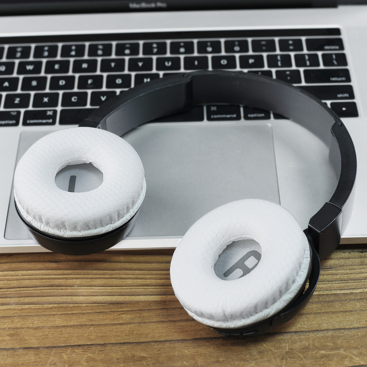 Auriculares blancos sobre teclado de portátil y mesa de madera.