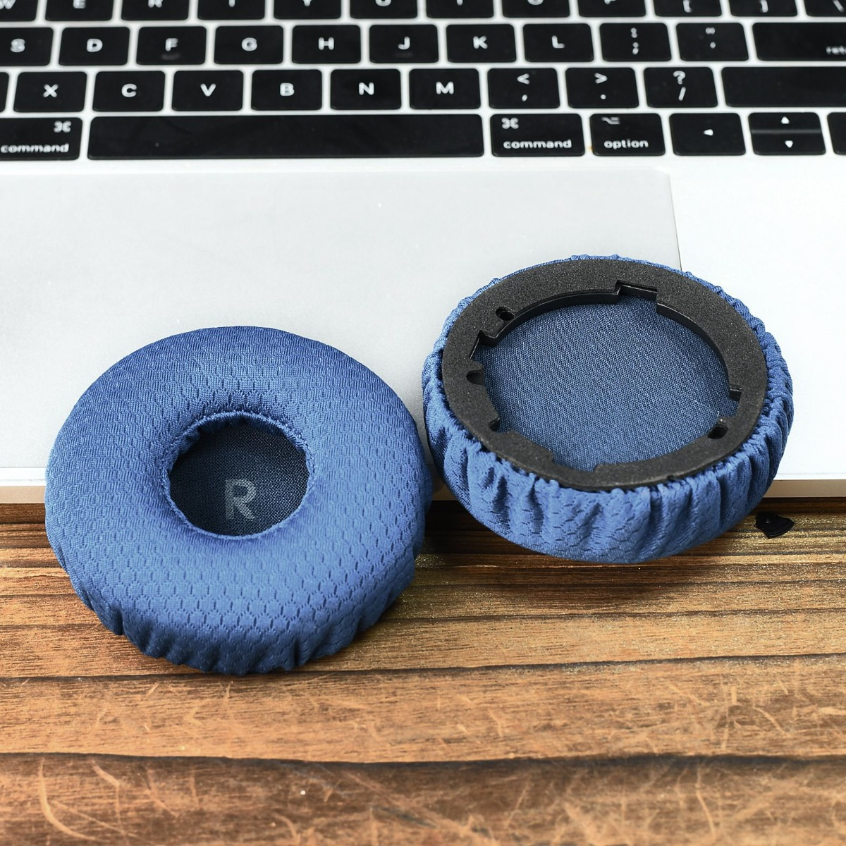 Dos almohadillas azules para auriculares descansan sobre un portátil y mesa de madera.