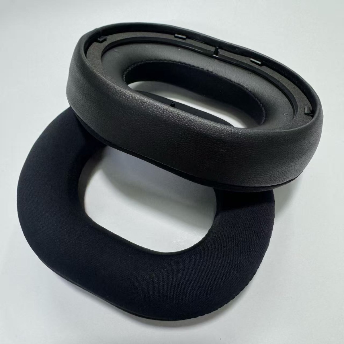 Dos almohadillas de auriculares negras, una de cuero sintético, la otra de tela.