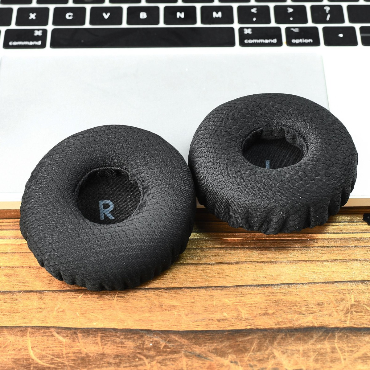 Dos almohadillas negras para auriculares descansan sobre un portátil y mesa de madera.