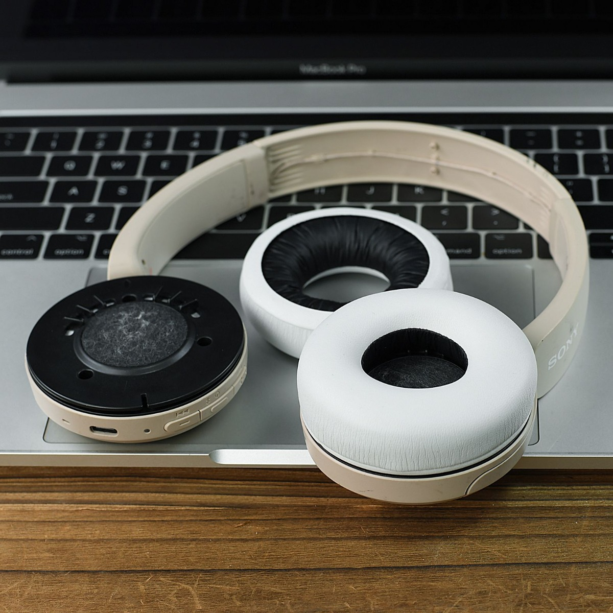 Auriculares blancos desmontados sobre teclado y mesa de madera.