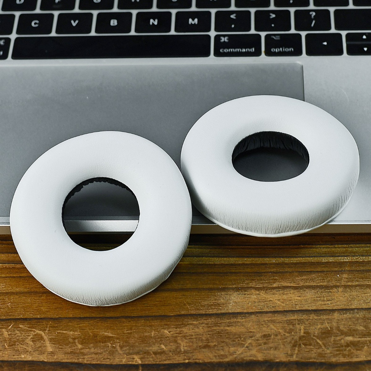 Dos almohadillas blancas para auriculares sobre un portátil y mesa.