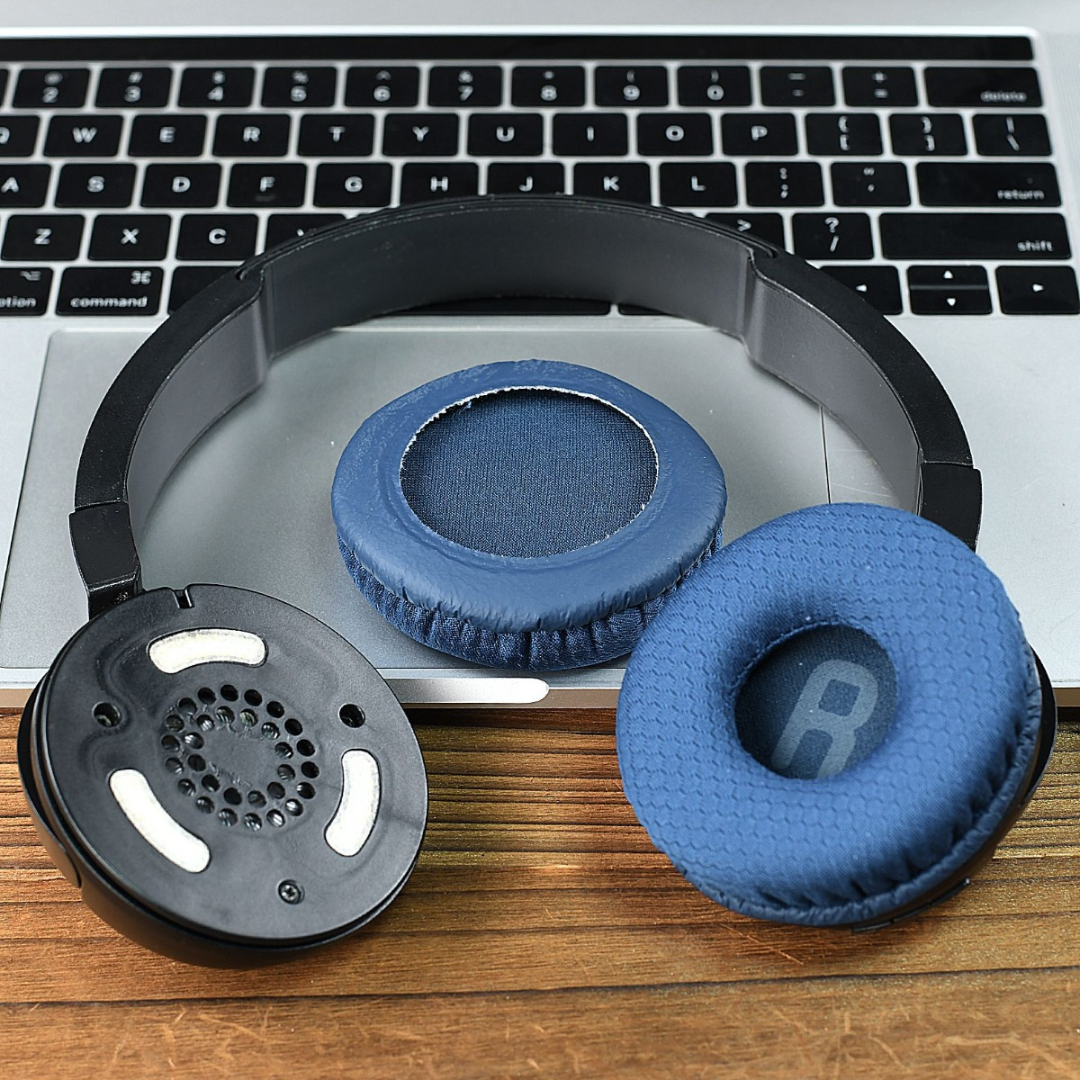 Auriculares azules descansan sobre un teclado de portátil y mesa de madera.