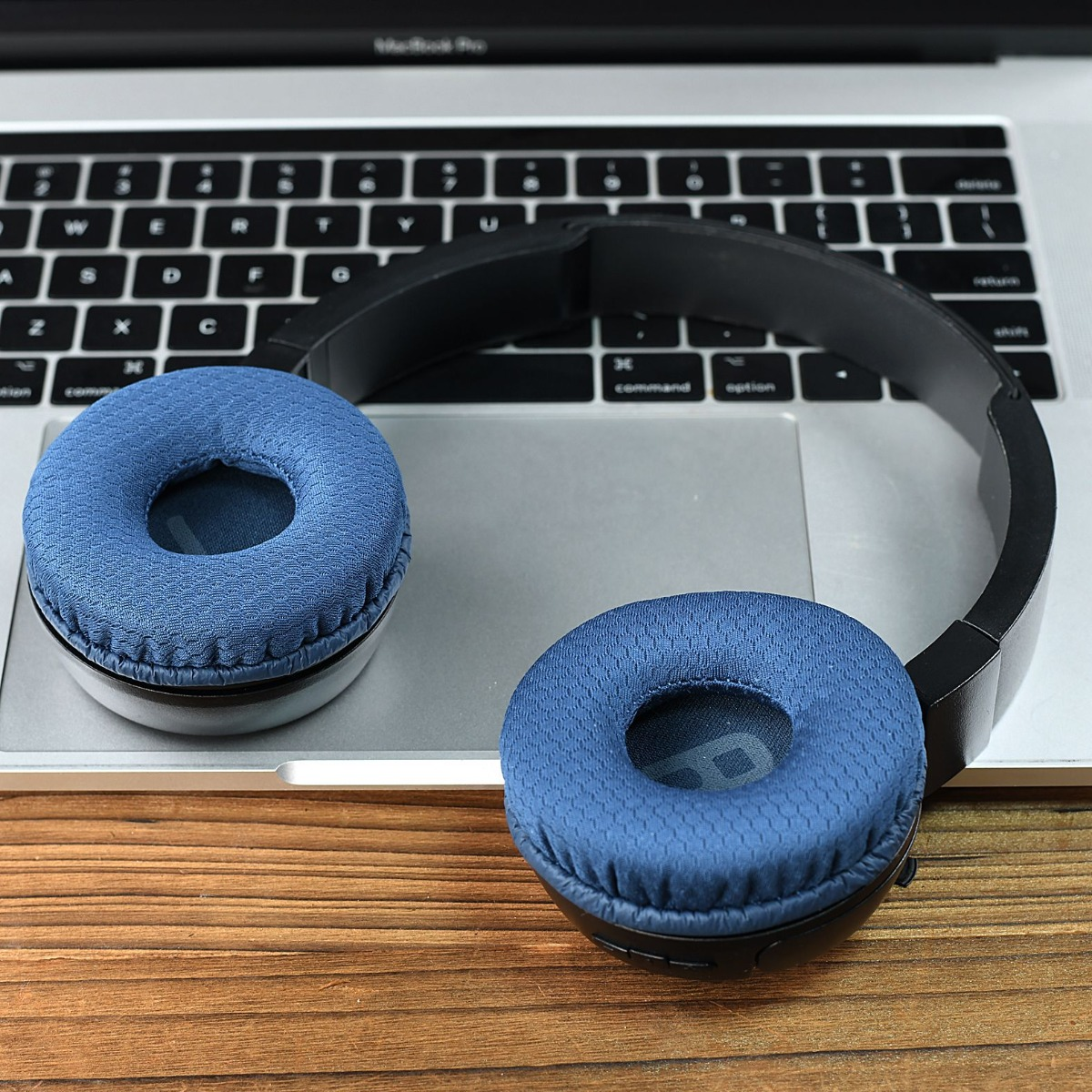 Auriculares azules sobre teclado de portátil. Superficie de madera.