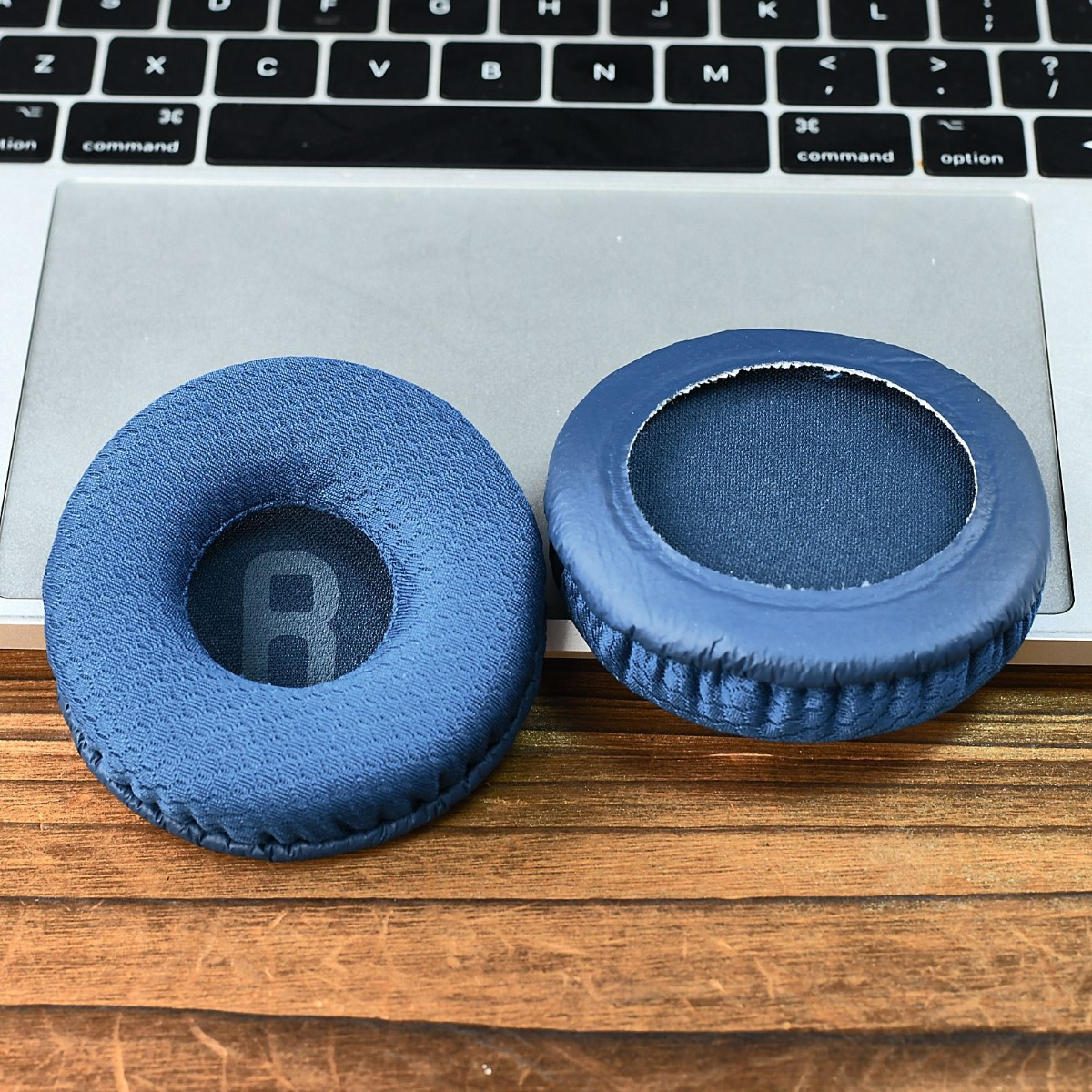 Dos almohadillas azules para auriculares descansan sobre un teclado y mesa de madera.