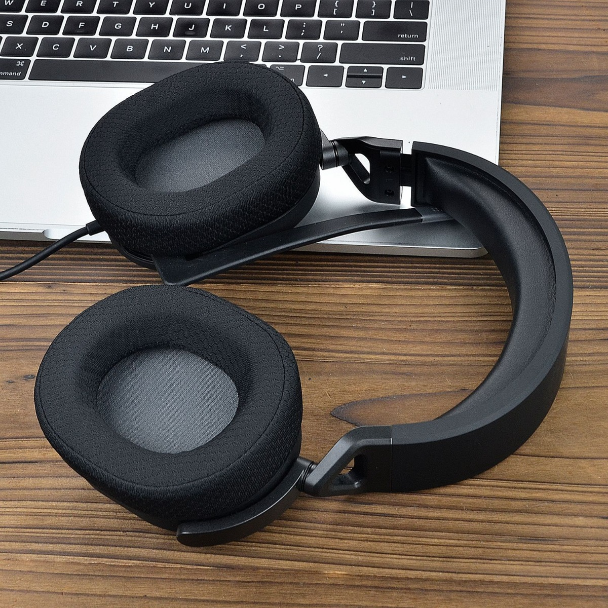Auriculares negros descansan sobre un teclado y mesa de madera.