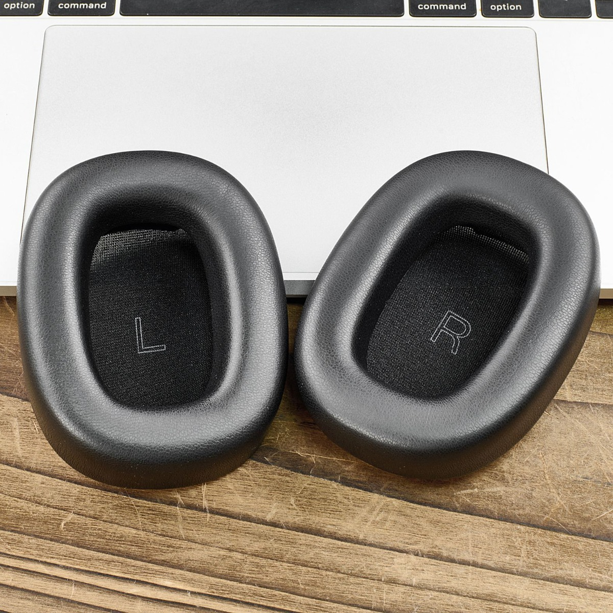 Dos almohadillas negras para auriculares, L y R, sobre una superficie de madera.