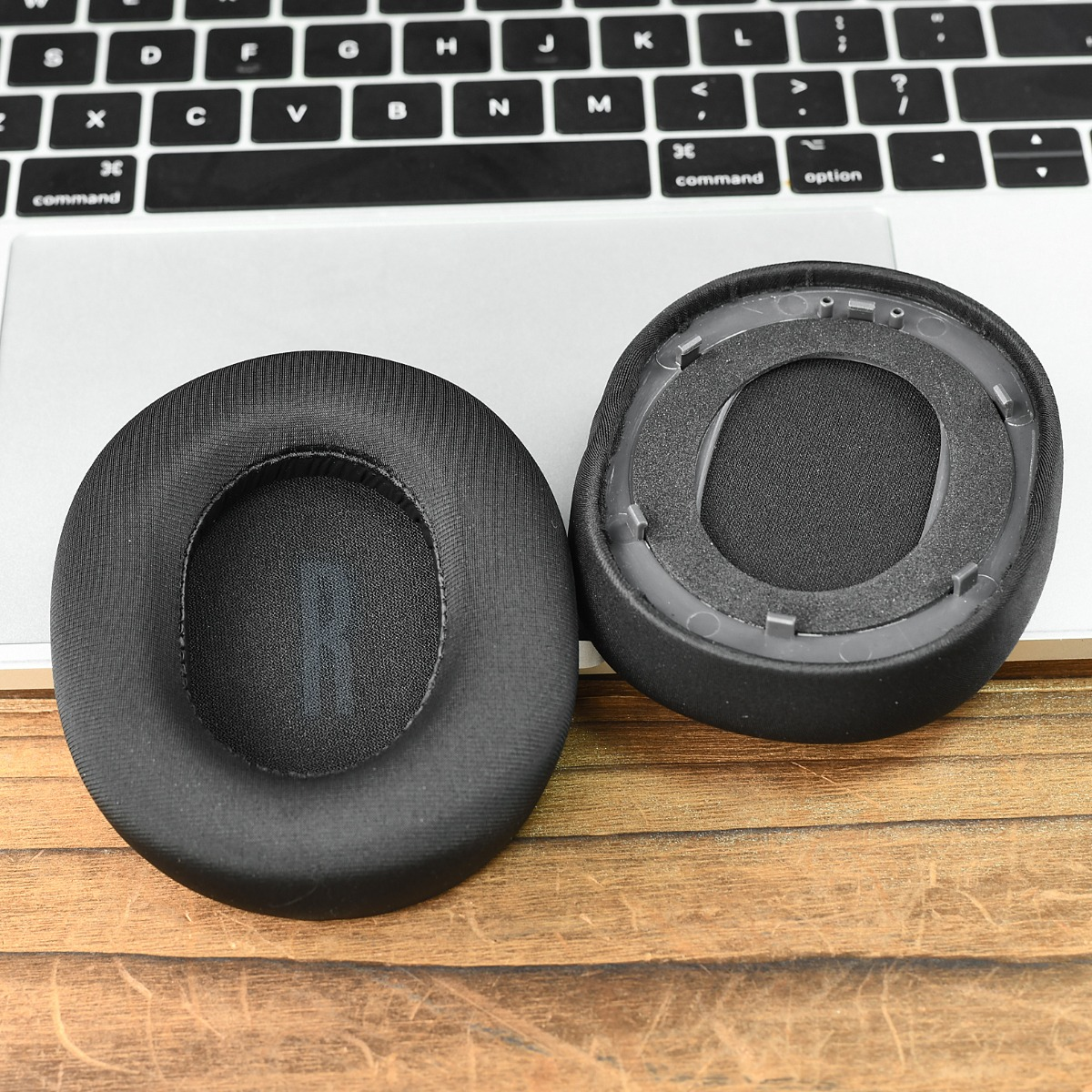 Dos almohadillas negras para auriculares descansan sobre un portátil y una mesa de madera.