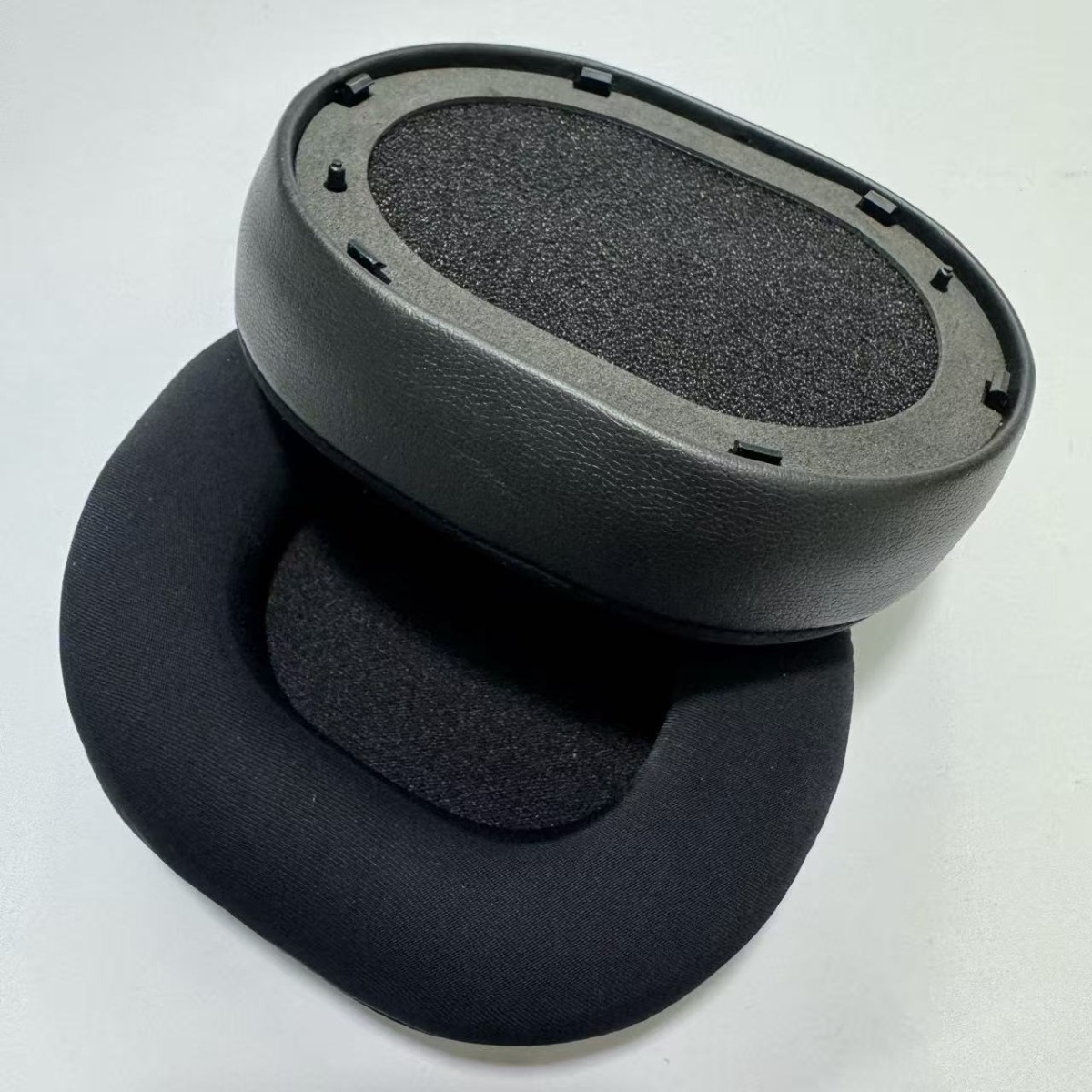 Almohadillas negras para auriculares, con espuma en el interior, sobre fondo blanco.