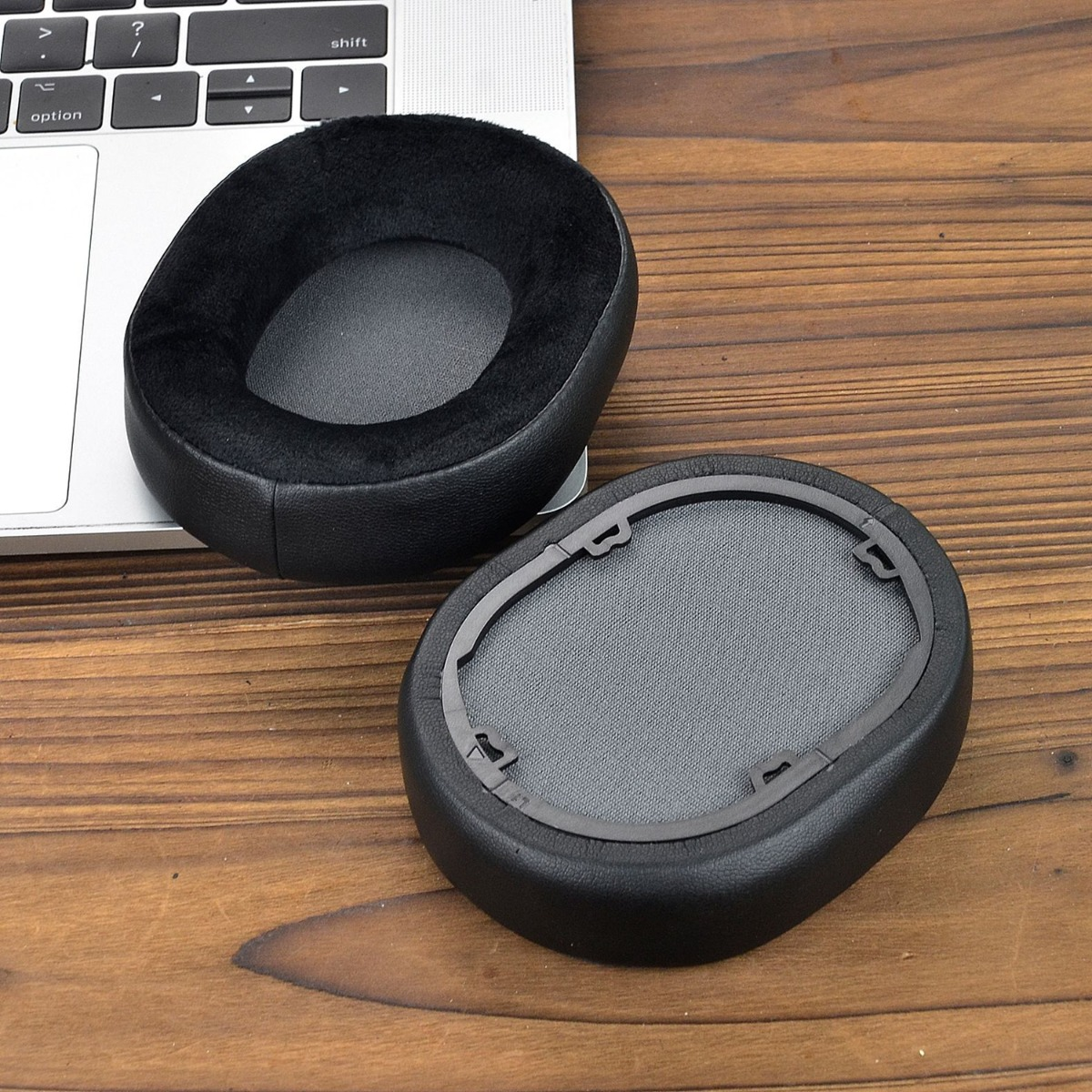 Dos almohadillas negras para auriculares descansan sobre un portátil y mesa de madera.