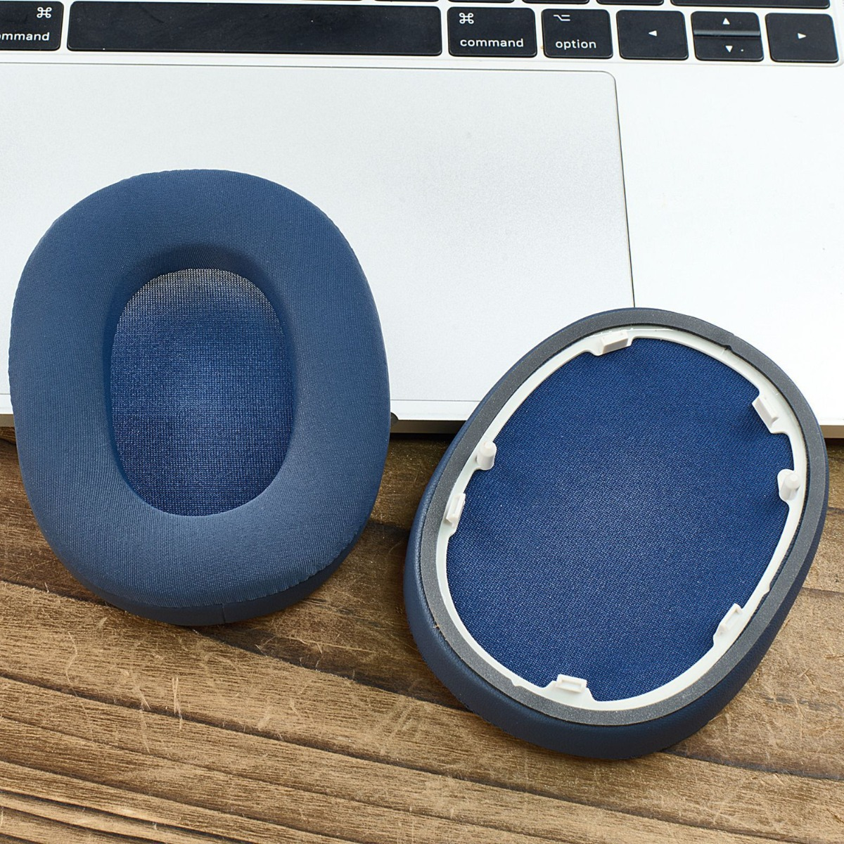 Zwei blaue Kopfhörerpolster liegen auf einem Holztisch, eine Tastatur im Hintergrund.