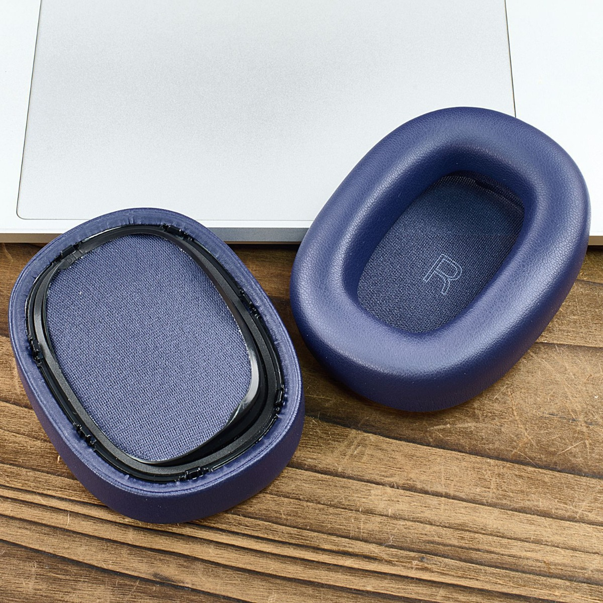 Dos almohadillas azules para auriculares sobre una mesa de madera, una marcada con 'R'.